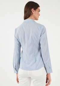 Camicia a maniche lunghe a righe blu e bianche con una vestibilità su misura, caratterizzata da un colletto classico e polsini abbottonati. Tessuto liscio con una sottile texture.