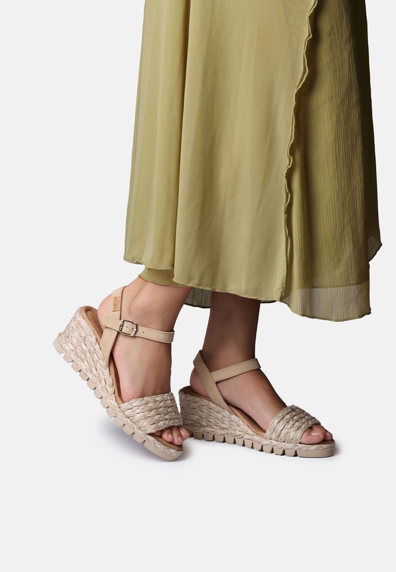 Beige sleehakken met geweven raffia-details, verstelbare enkelband en een gestructureerde zool. Gecombineerd met een vloeiende groene jurk.