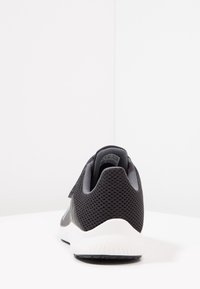 Chaussure de sport en maille noire avec une surface texturée, présentant une semelle intermédiaire blanche et une semelle extérieure en caoutchouc noir. Design minimaliste avec une languette à l'arrière.