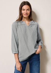 Blouse rayée avec un décolleté en V, des manches trois-quarts et des détails de manches bouffantes. Le tissu semble léger avec une texture douce en bleu marine et blanc.