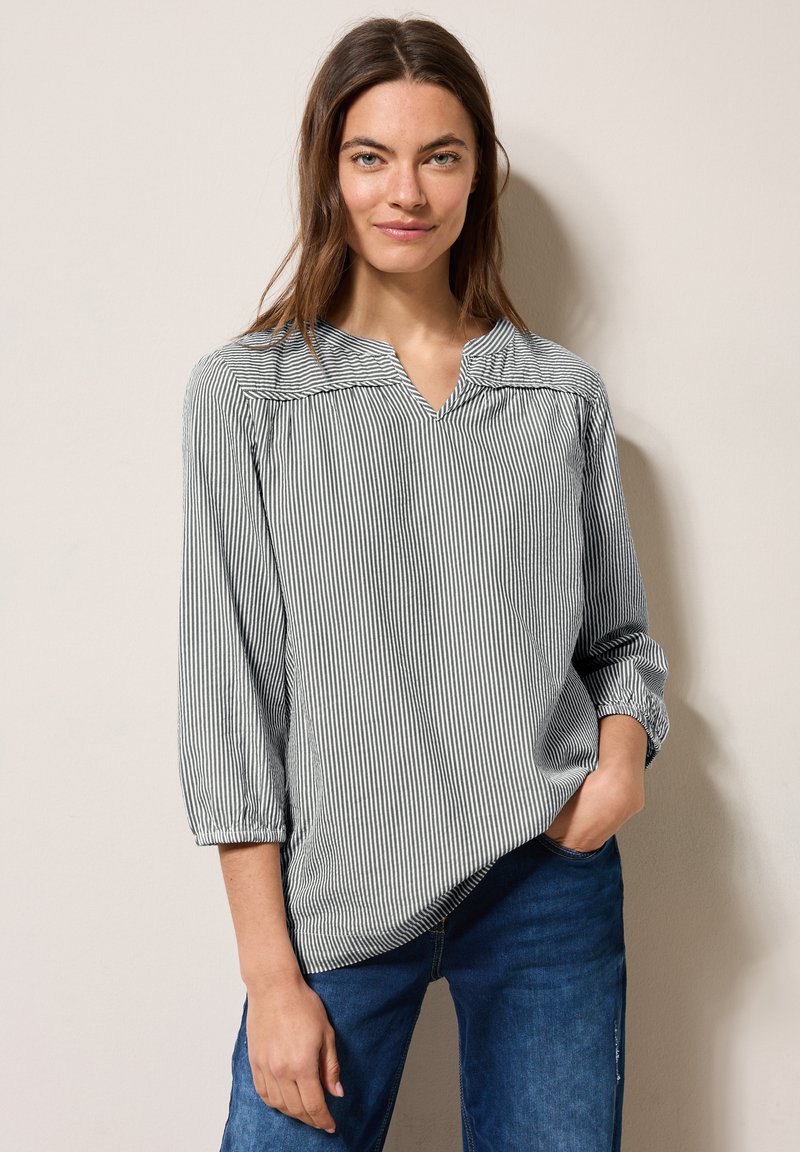 Blouse rayée avec un décolleté en V, des manches trois-quarts et des détails de manches bouffantes. Le tissu semble léger avec une texture douce en bleu marine et blanc.