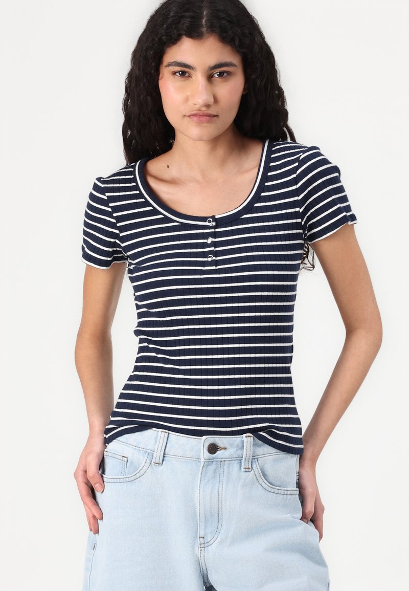 T-shirt côtelé bleu marine avec des rayures blanches horizontales, col arrondi, manches courtes et patte de boutonnage à trois boutons à l'avant.