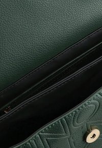 Intérieur d'un sac à main en cuir texturé vert avec une doublure noire, comprenant un compartiment zippé et une fermeture à bouton en métal doré.