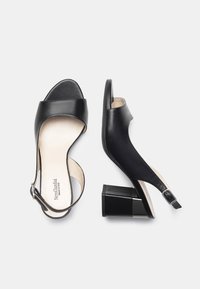 Sandali in pelle nera con una larga fascia superiore, punta aperta e cinturino alla caviglia regolabile. Il tacco quadrato offre stabilità. Texture morbida.
