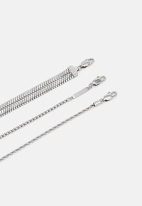 Tre catene d'argento: una con motivo a lisca di pesce, una con maglie rotonde semplici e una con design intrecciato, ciascuna con una chiusura sicura.