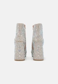 Bejeweled ankle boots featuring a textured surface adorned with iridescent small beads, a tan zipper, and a chunky heel for stability.