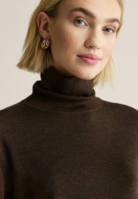 Brun polotröja i mjukt stickat tyg med en texturerad yta. Guldörhängen i form av hoops kompletterar looken och tillför en raffinerad detalj.
