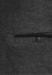 Dunkelgrauer Stoff mit weicher Textur verfügt über eine horizontale Tasche mit einem schwarzen Knopfakzent. Dezentes Muster im Material.