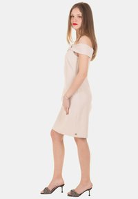 Abito beige off-the-shoulder realizzato in tessuto morbido, lunghezza fino a metà coscia, con un sottile accento di logo e abbinato a sandali neri con tacco a fantasia.