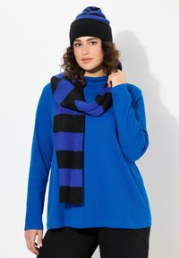 Maglione blu a maniche lunghe con collo alto, abbinato a una sciarpa a righe nera e viola e un berretto coordinato. Tessuti a maglia texturizzati.
