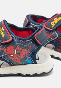 Lasten sandaalit, jotka on varustettu laivaston sinisellä ja punaisella muotoilulla, Spider-Man -grafiikalla ja tarrakiinnityksellä. Pehmeä pohja, jossa on teksturoitu kulutuskuvio.