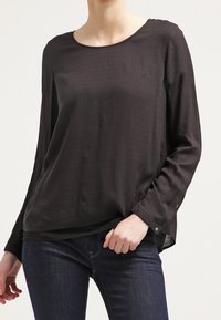 Sort langærmet bluse med rund halsudskæring, der har en løs pasform og et subtilt struktureret mønster. Sammen med mørke jeans.