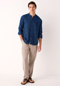 Blauw patroon overhemd met knopen en opstaande kraag, enkele borstzak, gecombineerd met lichtbeige broek en bruine slippers.