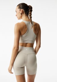 Brassière de sport beige et shorts taille haute en matériau doux et extensible. Design sans coutures avec un logo discret à l'arrière. Coupe sculptante.