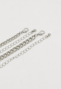 Trois chaînes en argent avec des tailles de maillons variées : une grande chaîne en curb épaisse, une petite chaîne à maillons ronds et une chaîne plus courte avec des fermoirs en métal.