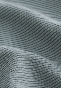 Sivi pleteni materijal s horizontalnim rebrastim uzorkom i mekim naborima koji stvaraju valoviti uzorak preko površine.