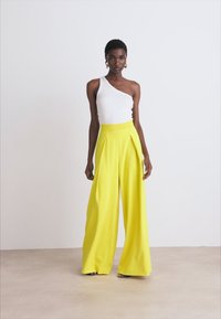 Witte één-schoudertop gecombineerd met felgele wijde broek met plooien, gemaakt van een lichtgewicht stof met een gladde textuur.