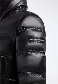 Zwarte pufferjack gemaakt van glanzende, gewatteerde stof met een capuchon. Beschikt over een logopatch op de mouw en elastische naden voor een goede pasvorm.