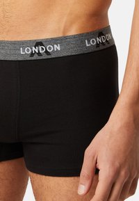 Black boxer shorts with a gray elastic waistband featuring the text "LONDON." The fabric is smooth with a fitted design and precise stitching.