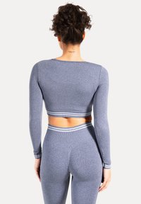 Blå langærmet croptop med en tætsiddende pasform, parret med matchende højtaljede leggings, der har stribede detaljer på ærmekanter og linning.