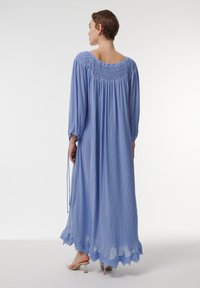 Vestido largo plisado de color azul claro con escote fruncido, mangas largas y borde de encaje en el dobladillo. Llevado con sandalias de tacón transparente.