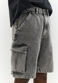 Shorts cargo en denim noir délavé avec une poche à rabat sur le côté, dotés de coutures classiques et d'une coupe droite.