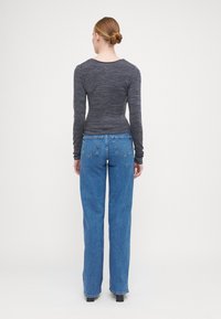 Haut ajusté à manches longues de couleur gris foncé associé à un jean bleu à jambe droite. Coutures visibles et deux poches arrière sur le jean.