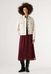 Balta džinsinė striukė su keturiomis kišenėmis, derinama su bordo spalvos su taškeliais maxi suknele. Juodi kelių ilgio batai užbaigia aprangą.