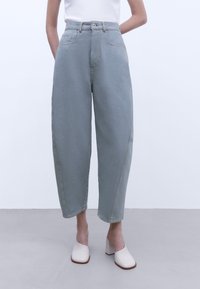 Lyseblå højtaljede denimbukser med løs pasform, der har forlommer, lige ben og gule syninger.