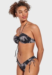 Top de bikini bandeau negro con estampado animal blanco, que cuenta con un centro anudado y lazos ajustables. Las braguitas tienen lazos laterales y un patrón a juego.