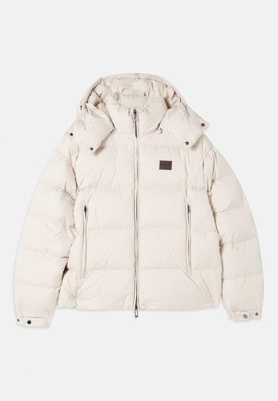 Beige pufferjakke med aftagelig hætte, lynlås foran og to sidelommer. Har quiltet design med stikninger og justerbare manchetter.