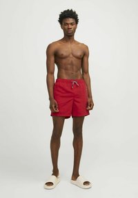 Bañador rojo con cintura elástica y cordón, con una textura suave. Se lleva con sandalias de colores claros.