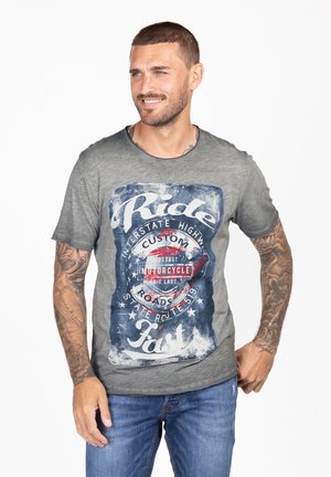 Camiseta gris con un gráfico de motocicleta vintage en rojo y azul, con texto y acentos desgastados. Mangas cortas y cuello redondo.
