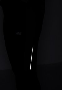 Czarne legginsy sportowe z odblaskowym białym paskiem i logo. Wykonane z gładkiego, elastycznego materiału zapewniającego komfort i swobodę ruchów.