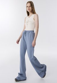 Pantalones de chándal de un azul claro, con un corte holgado y una cinturilla elástica, que cuentan con costuras laterales con pequeños adornos decorativos y bolsillos.