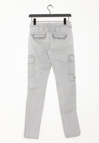 Ljusgrå cargobyxor med klafffickor och knappdetaljer hängande på en svart byxhanger mot en vit bakgrund.