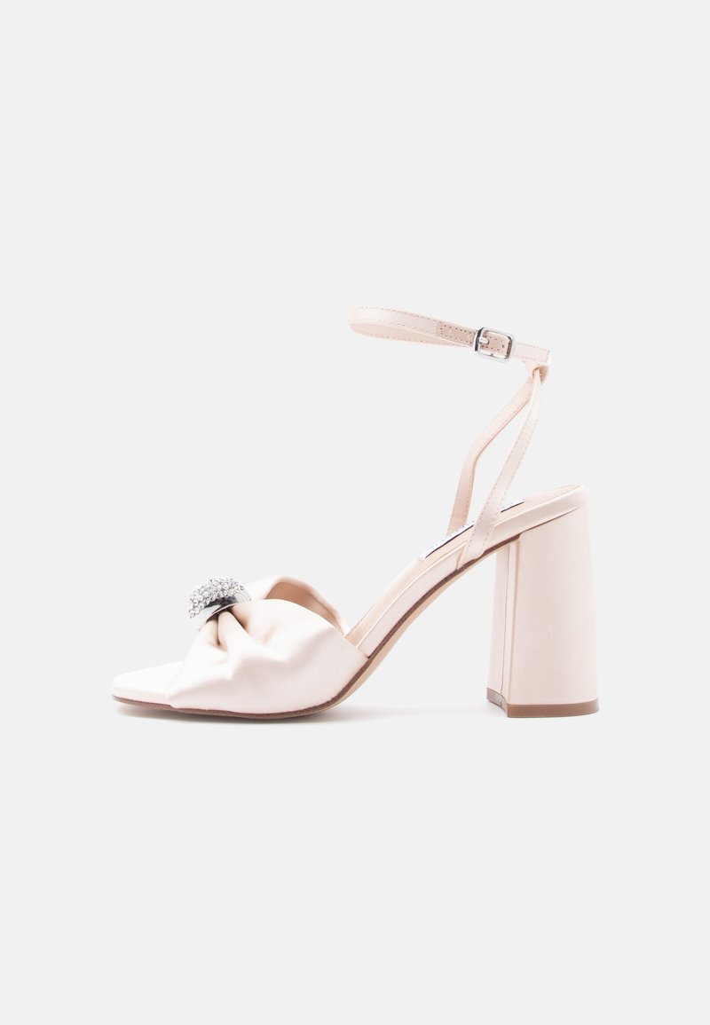 Sandalia de satén rosa pálido con un diseño anudado, adornada con un detalle de circonitas y un tacón grueso y resistente para mayor estabilidad.