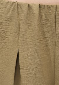 Μπεζ υφασμάτινη φούστα με εμπρόσθια σχίση, που παρουσιάζει υφή, ελαφρώς ζαρωμένο υλικό και μια διακριτική έκθεση δέρματος πάνω από τη μέση.