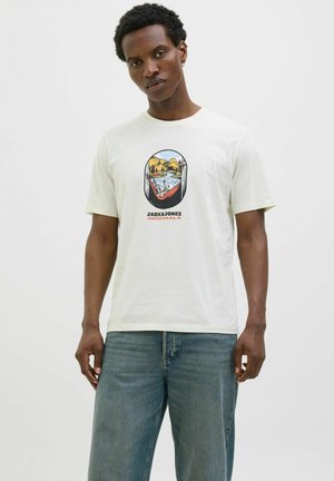 Hvid bomulds T-shirt med en grafisk print, der viser bjerge og vand, korte ærmer og en rund halsudskæring, parret med lyseblå jeans.