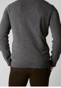 Šedý pletený svetr s žebrovaným lemem a manžetami, který má hladkou texturu a klasický design s kulatým výstřihem. Nosený přes hnědé kordové kalhoty.