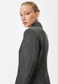 Blazer in tweed black e bianco su misura con colletto strutturato, tessuto testurizzato e rever a punta, dotato di uno spacco posteriore singolo.