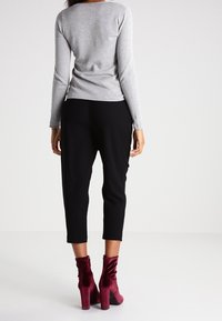 Top grigio a maniche lunghe abbinato a pantaloni neri alla caviglia e stivali con tacco color borgogna. Tessuto morbido, design aderente e silhouette con tacco alto.