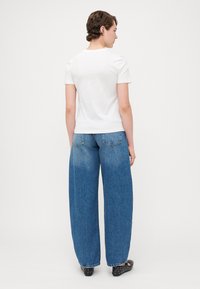 Witte t-shirt met korte mouwen, gecombineerd met losse, vervaagde blauwe wide-leg jeans. De jeans hebben een standaard vijf-pocket ontwerp met zichtbare stiksels.