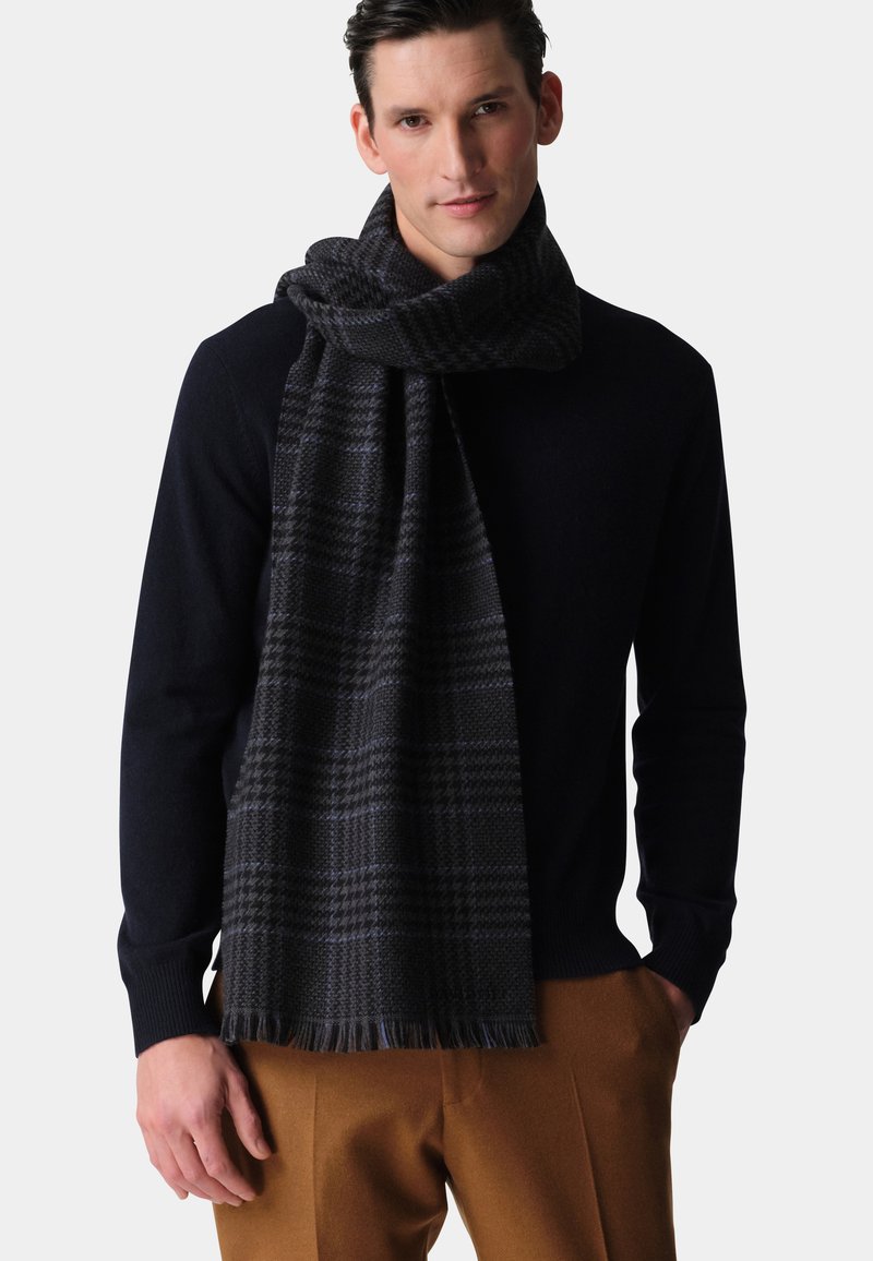 Dunkler karierten Schal aus weichem Stoff mit fransigen Kanten, getragen über einem marineblauen Pullover. Einfaches und modernes Design mit strukturierter Oberfläche.