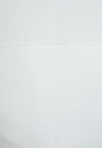 Weißer Baumwollstoff mit glatter Textur, der ein flaches Nahtdetail entlang der horizontalen Mitte aufweist. Minimalistisches Design ohne Muster.