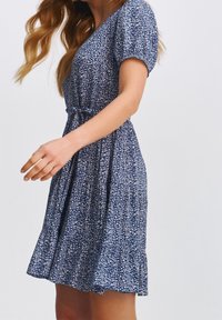 Kwiatowa sukienka w kolorze niebieskim z krótkimi bufkami, dopasowaną talią i rozkloszowanym dołem. Materiał zdobiony jest białym wzorem liści.