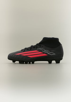 Schwarzer Fußballschuh mit roten Streifen, mittelhohem Schaft und geformten Stollen an der Sohle für das Spielen auf festem Boden.