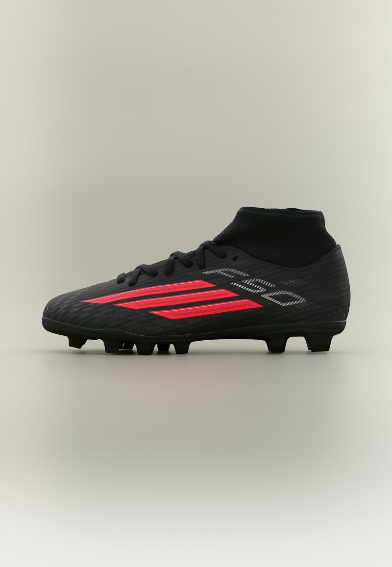Μαύρο ποδοσφαιρικό παπούτσι με κόκκινες ρίγες, μεσαίου ύψους κάλος κάλτσας και μορφοποιημένες σταμπωτές ακίδες στη σόλα για παιχνίδι σε στερεό έδαφος.