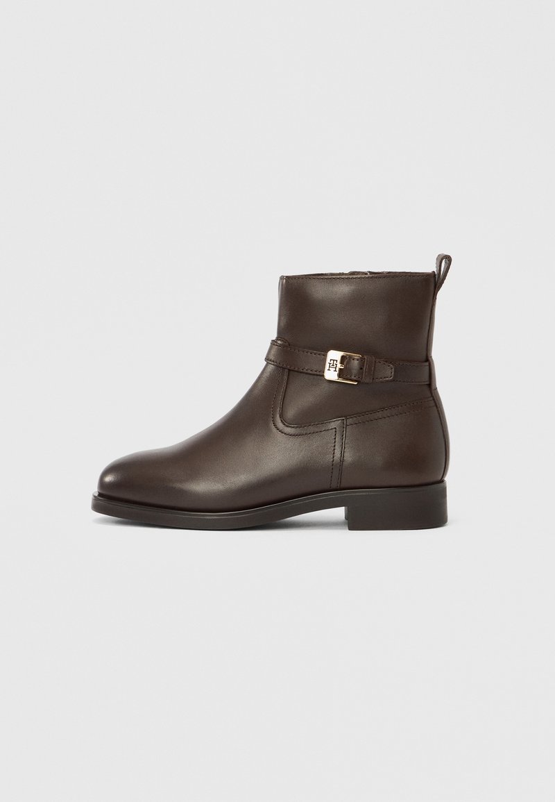 Bottine en cuir brun foncé avec petit talon, bride latérale à boucle et languette de préhension sur fond neutre.