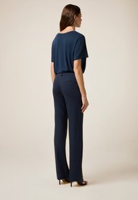 Haut ample bleu marine et pantalon bleu marine ajusté, présentant une texture lisse et des lignes épurées. Les chaussures incluent des talons aiguilles noirs à lanières.